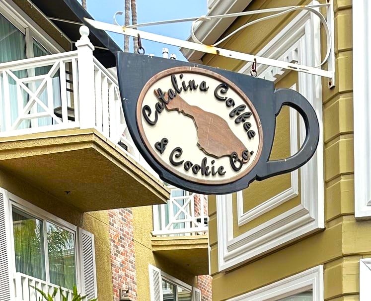 A large coffee cup-shaped store sign hanging from a mustard yellow building.