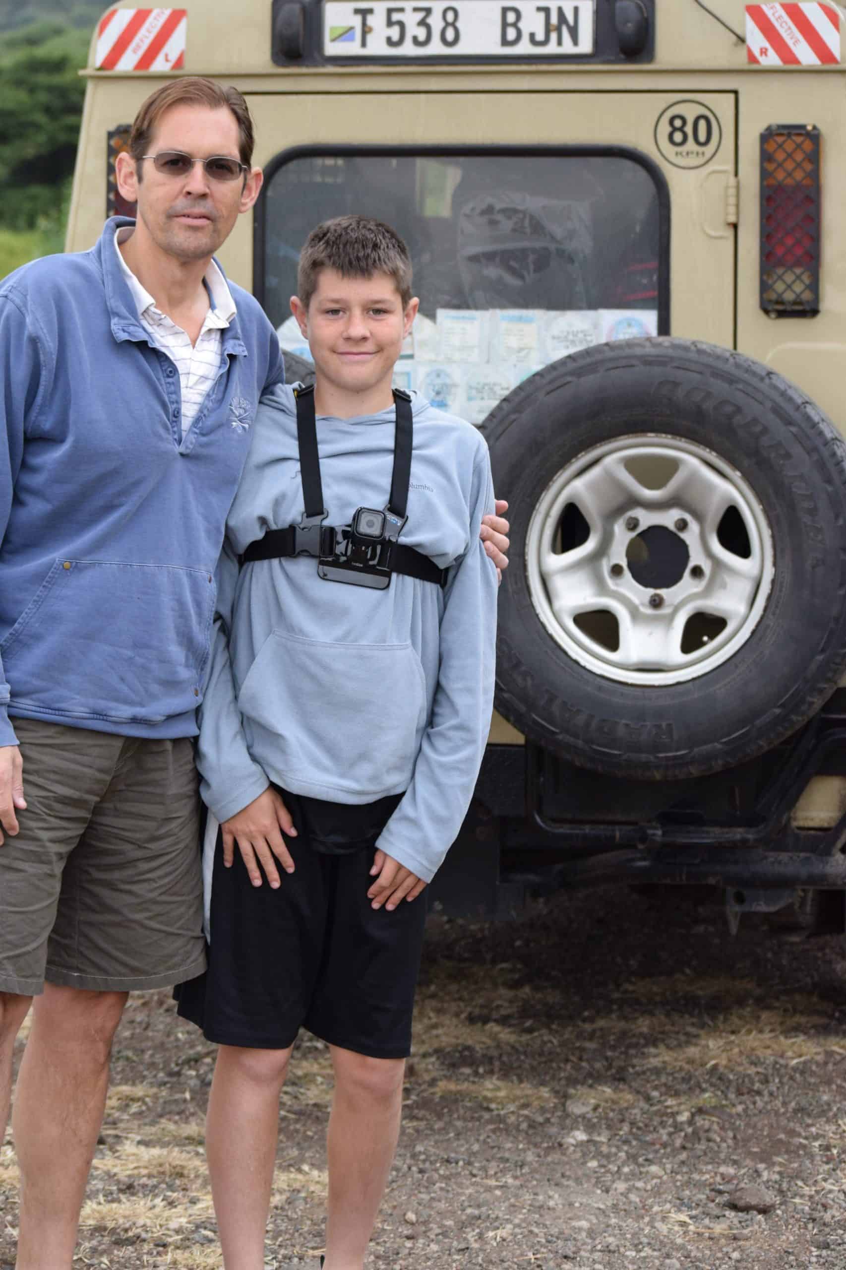 Man and boy, standing next to safari vehicle on safari in Africa.