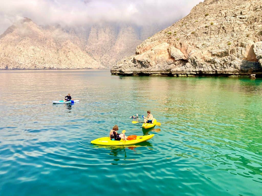Three yellow kayaks on calm waters with rocky mountains in background.