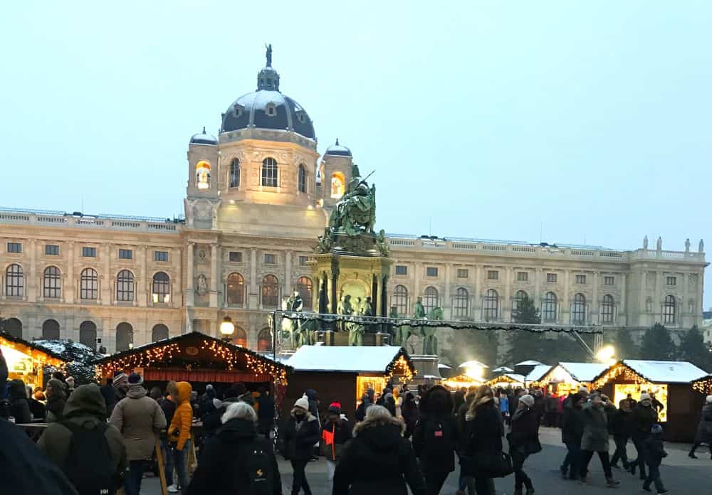 Wooden booths decorated for Christmas in front of large palace in Vienna in Winter.