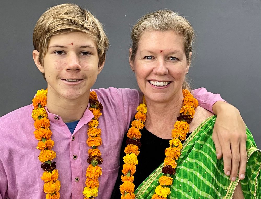 Teenaged boy and his mother, wearing marigold necklaces and Indian clothing, smiling toward the camera.
