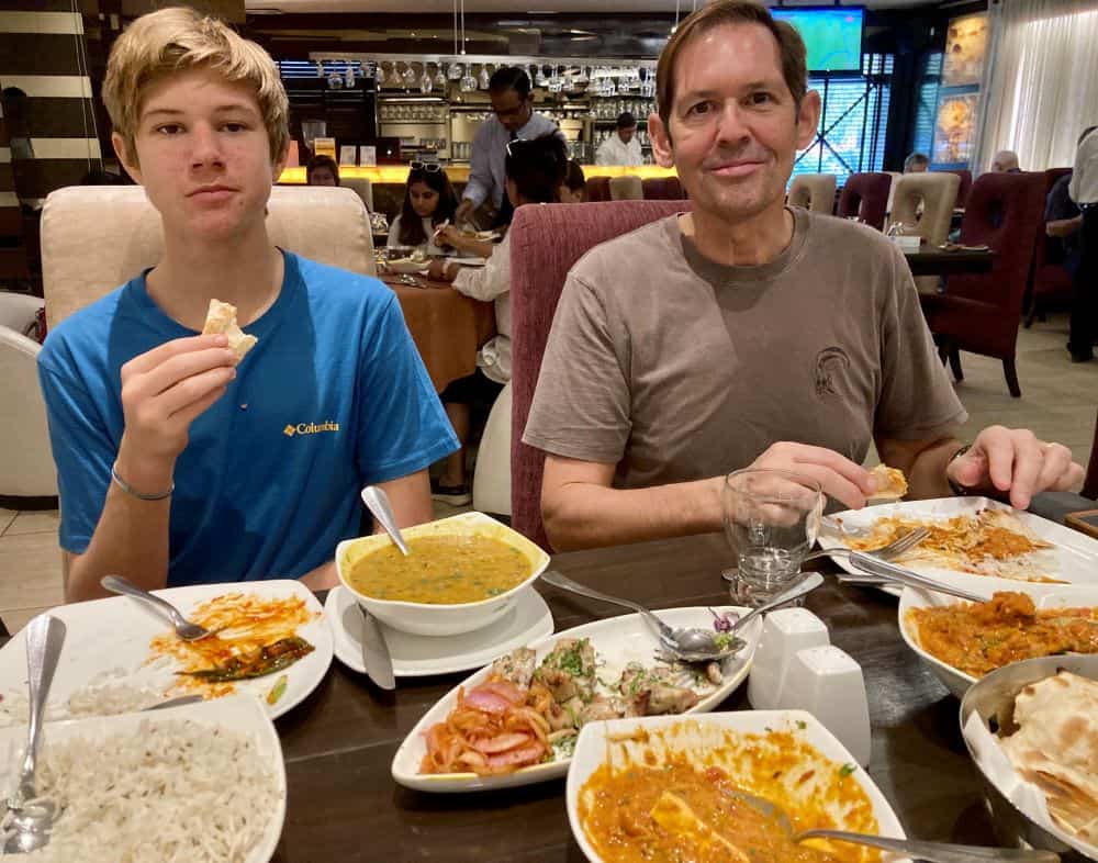 A father and son at a table with many dishes of traditional Indian food.