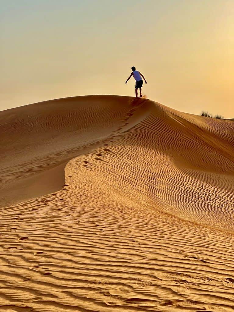 A boy climbing a sand dune at sunset