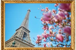 Tall metal tower rising into the blue sky, next to pink blooms on a tree. Surrounded by gold decorated frame.