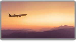 Airplane flying at sunset, over mountains in an orange sky.