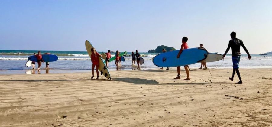 A group of young people walking across the beach with their surfboards, for their surfing in sri lanka beginner lesson.