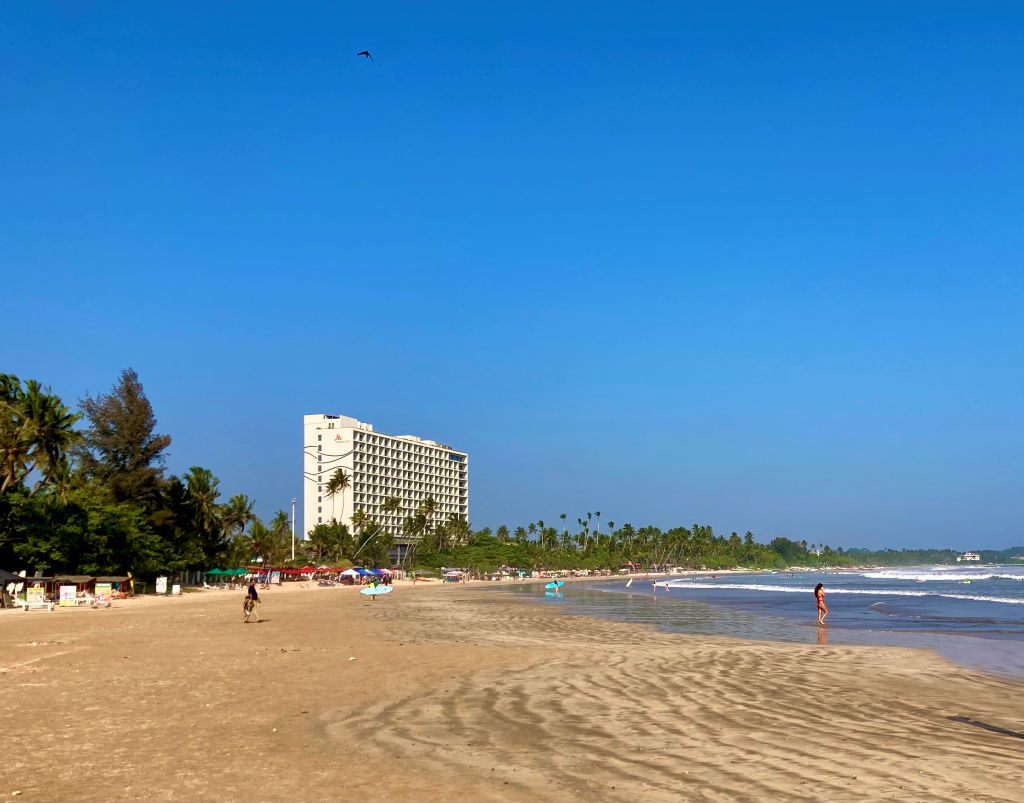 Tall hotel along the shoreline of a wide and sandy beach in Sri Lanka.