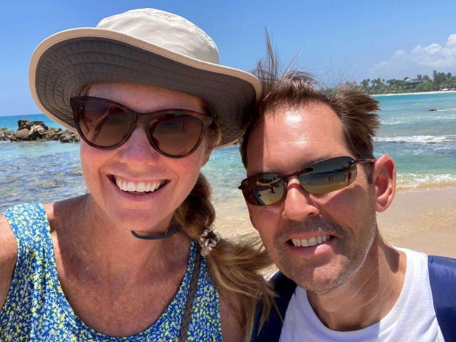 A man and a woman smiling on a sandy beach in Sri Lanka on a sunny day.