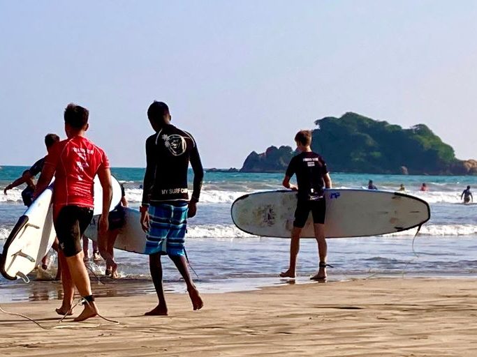 Boys with surfboards walking into the water at a calm beach in Sri Lanka