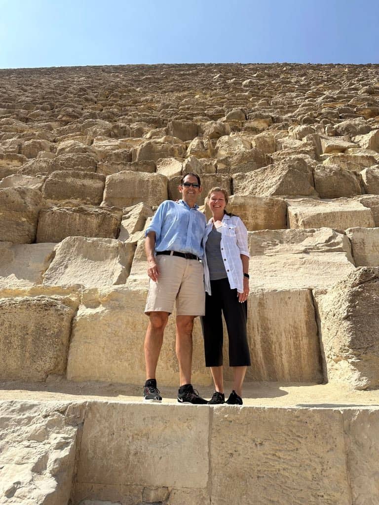 Two adults stand on large stones at the base of a steep pyramid in Cairo Egypt.
