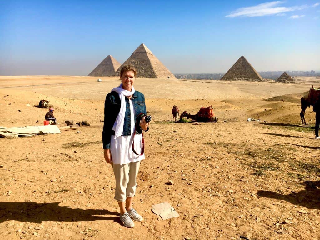 Woman standing in the desert in front of camels and the Pyramids on the Giza Plateau. Cairo is in the background.
