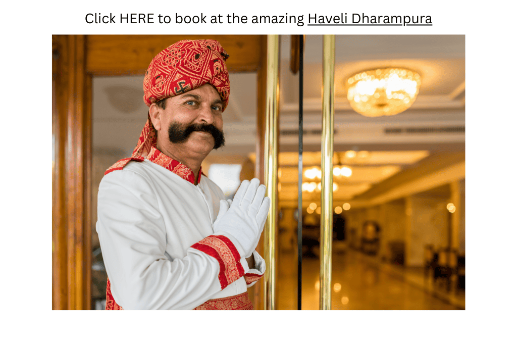 Man wearing a red head turban stands near a hotel entrance in New Delhi, India, with his hands together in greeting giving the perception that New Delhi is safe.