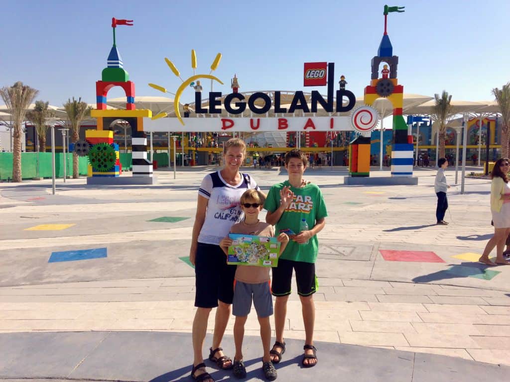 Mother and two sons stand in front of the Legoland Dubai entrance on a sunny day.