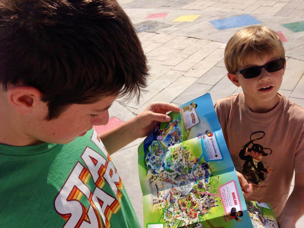 Two boys study a colorful map of Legoland Dubai, on a cement brick walkway.