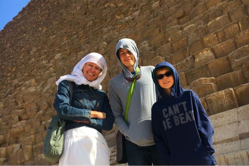 A mother with a white scarf over her head, stands with her two sons wearing hoodie sweatshirts in front of the Great Pyramid in Cairo, Egypt.