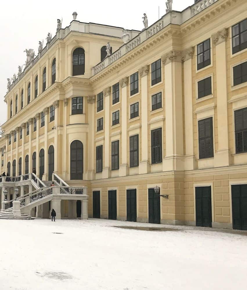 Big palace with creamy walls and multiple stories. Closed windows and doors on the side of the building closest to the photographer. Snow on the ground gives a cold feeling.