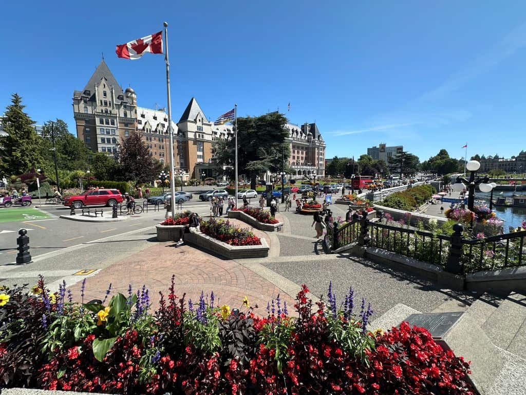A Canadian Flag flies in the foreground of a large building in Victoria on a sunny day.