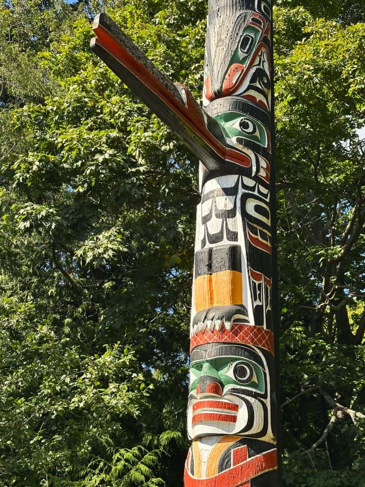 A colorful totem pole with an eagle beak decoration sticking out, in a park in Victoria, Canada.
