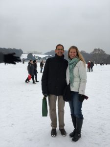 A man and woman standing in the snow under grey sky.