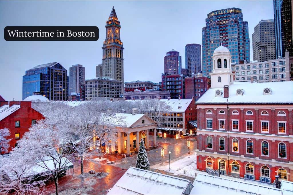 Snow-covered historic buildings and city skyline in downtown Boston during winter, showing festive lights, frosted trees, and a classic wintertime city scene. Text: Wintertime in Boston.