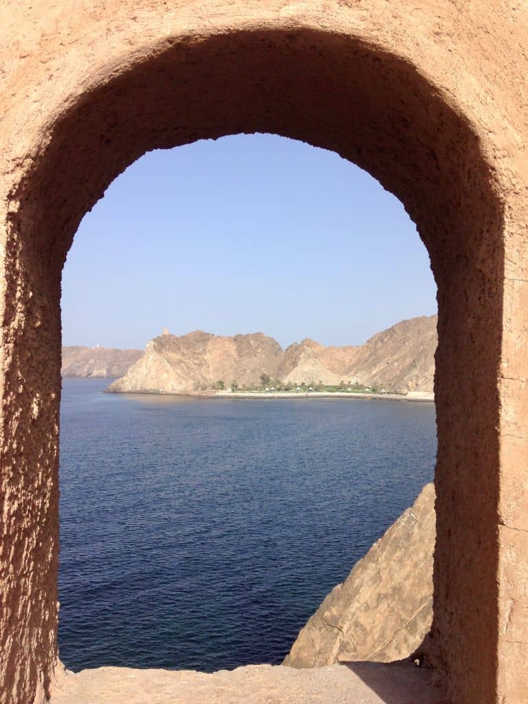 Rocky shoreline seen through an arched window of a stone fort in Oman.