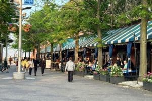 Outdoor waterfront cafés in Boston with people dining and walking along the Harborwalk, a great area to experience what to eat in Boston on a first visit.