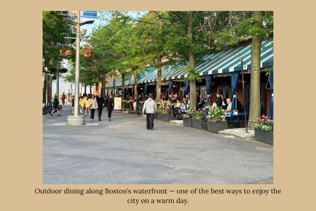 Outdoor cafés along Boston’s waterfront Harborwalk, with people strolling past tree-lined sidewalks and diners enjoying outdoor seating near the harbor.