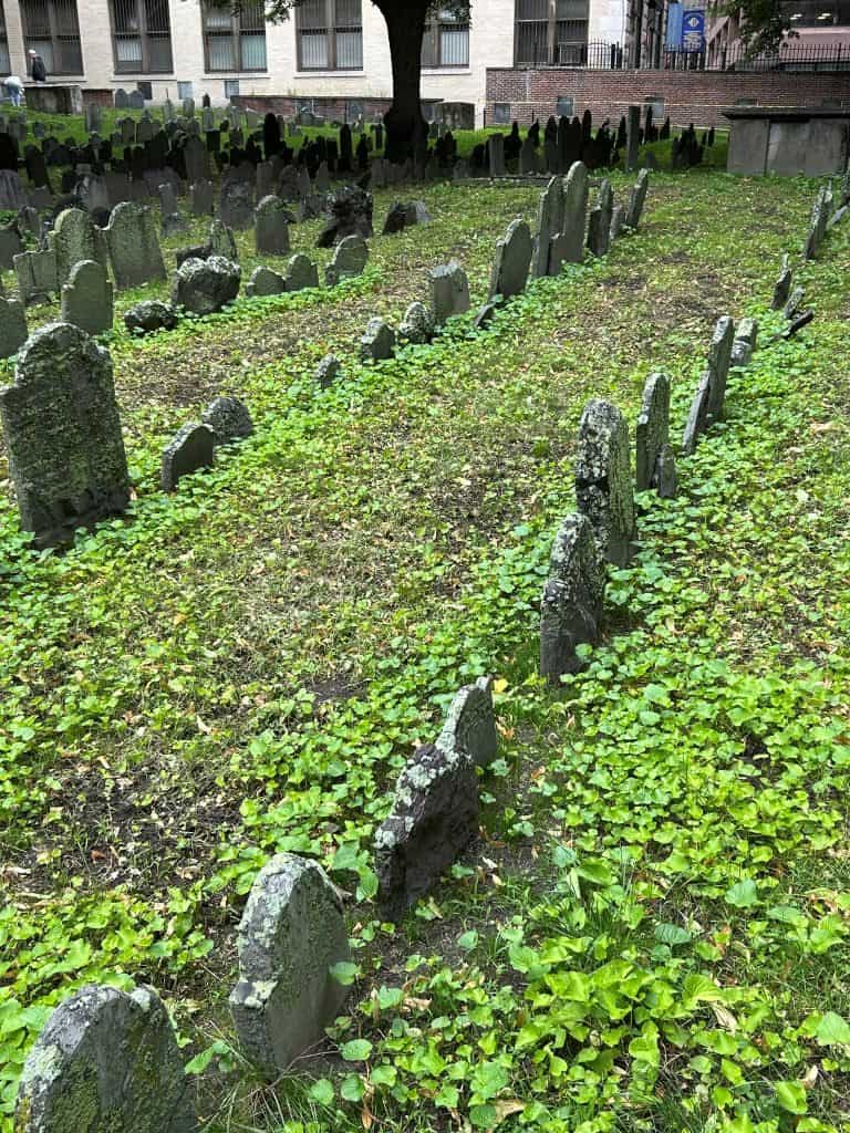 Dozens of old headstones in a lush, green graveyard in Boston.