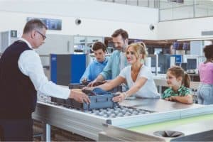 Family placing bags and items on airport security table with an airport agent helping.