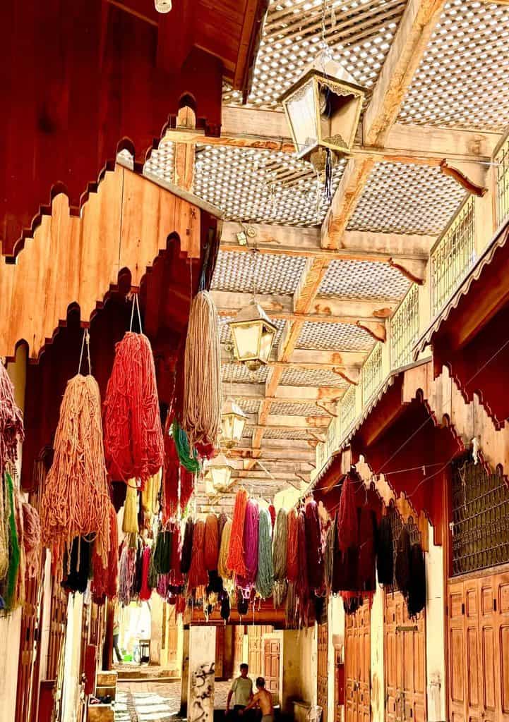 Narrow covered lane with colorful yarn hanging overhead in the Fes medina, Morocco.