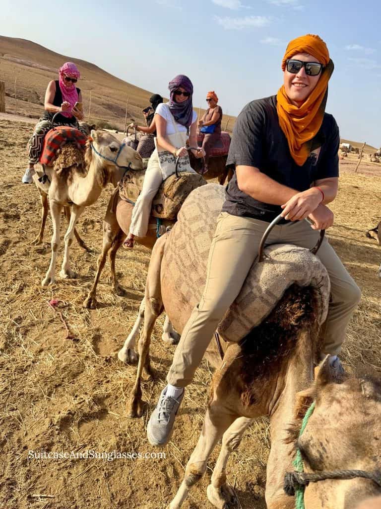 Tourists wearing colorful headscarves riding camels in a line through the rocky Agafay Desert near Marrakech, Morocco.