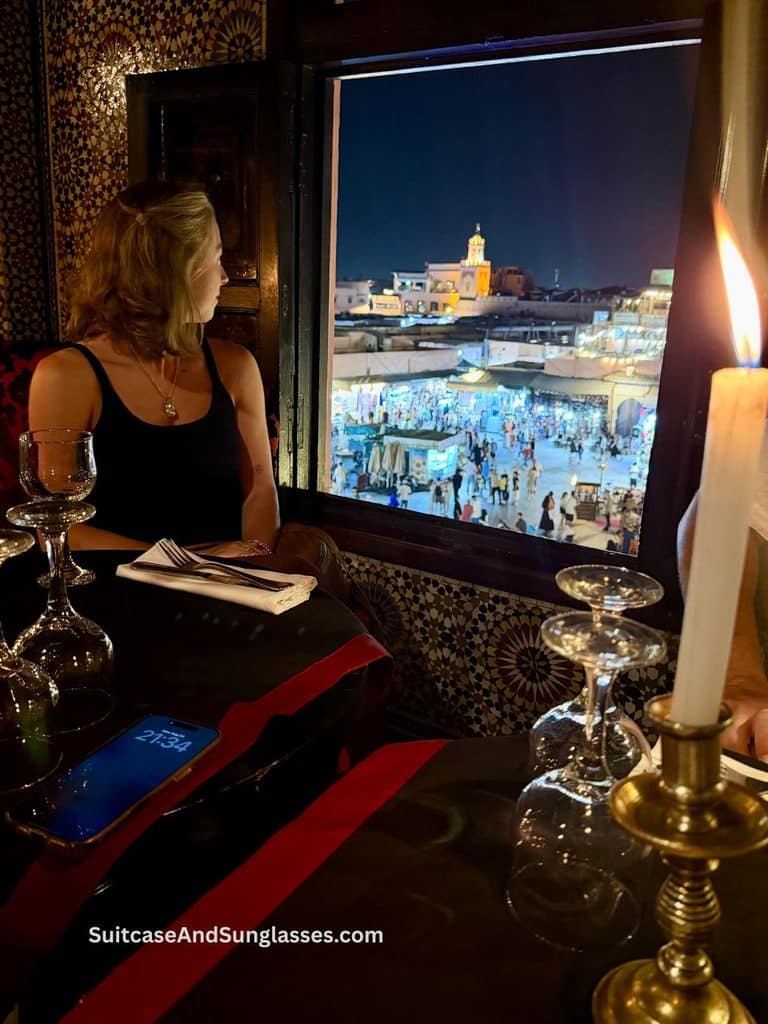 Candlelit window table at Le Marrakchi restaurant overlooking the illuminated Jemaa el-Fnaa square in Marrakech, Morocco, at night.